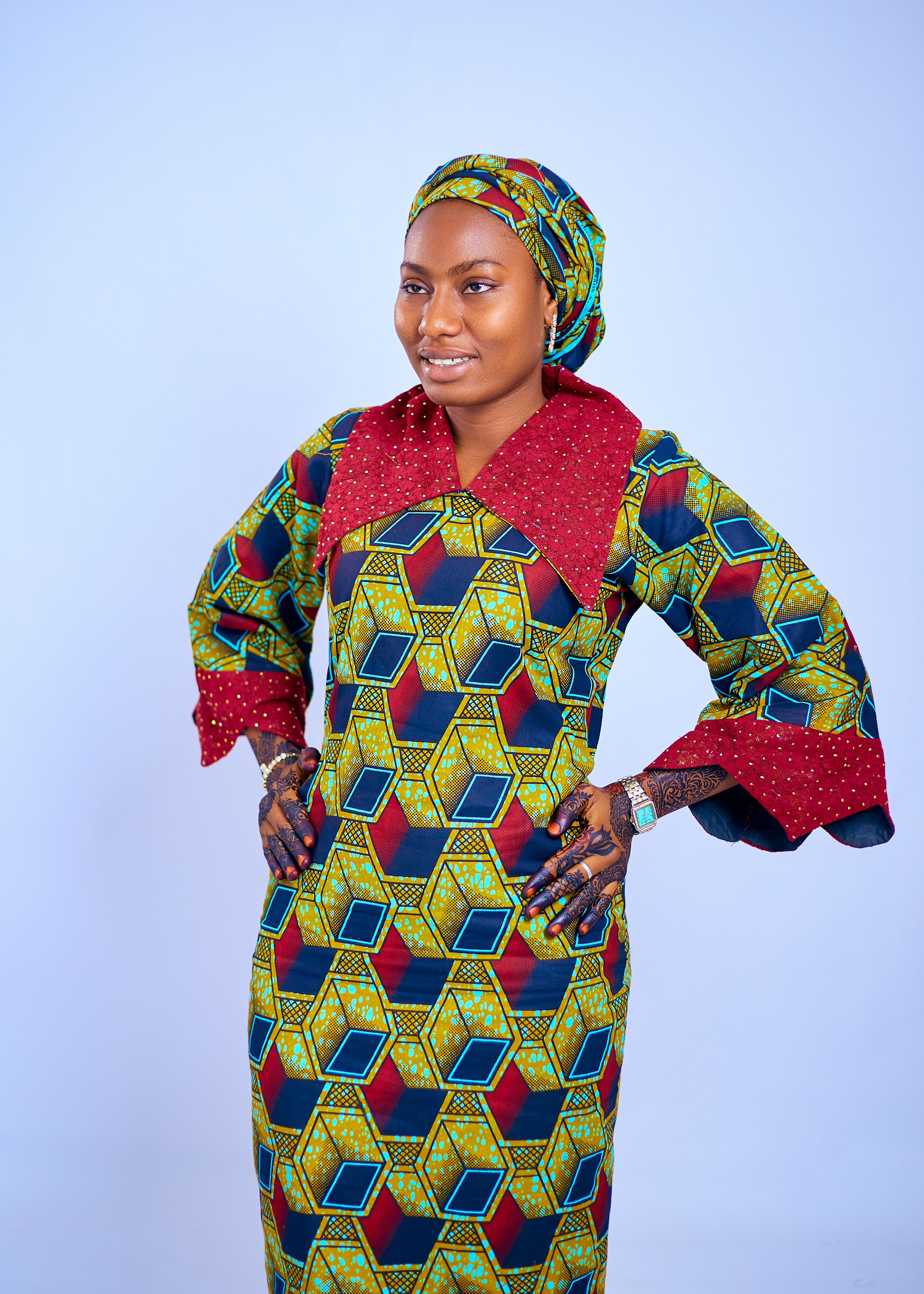 Smiling woman in vibrant African attire standing confidently against a blue backdrop.