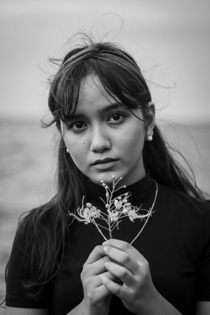 Captivating black and white portrait of a woman gazing intently while holding delicate flowers.