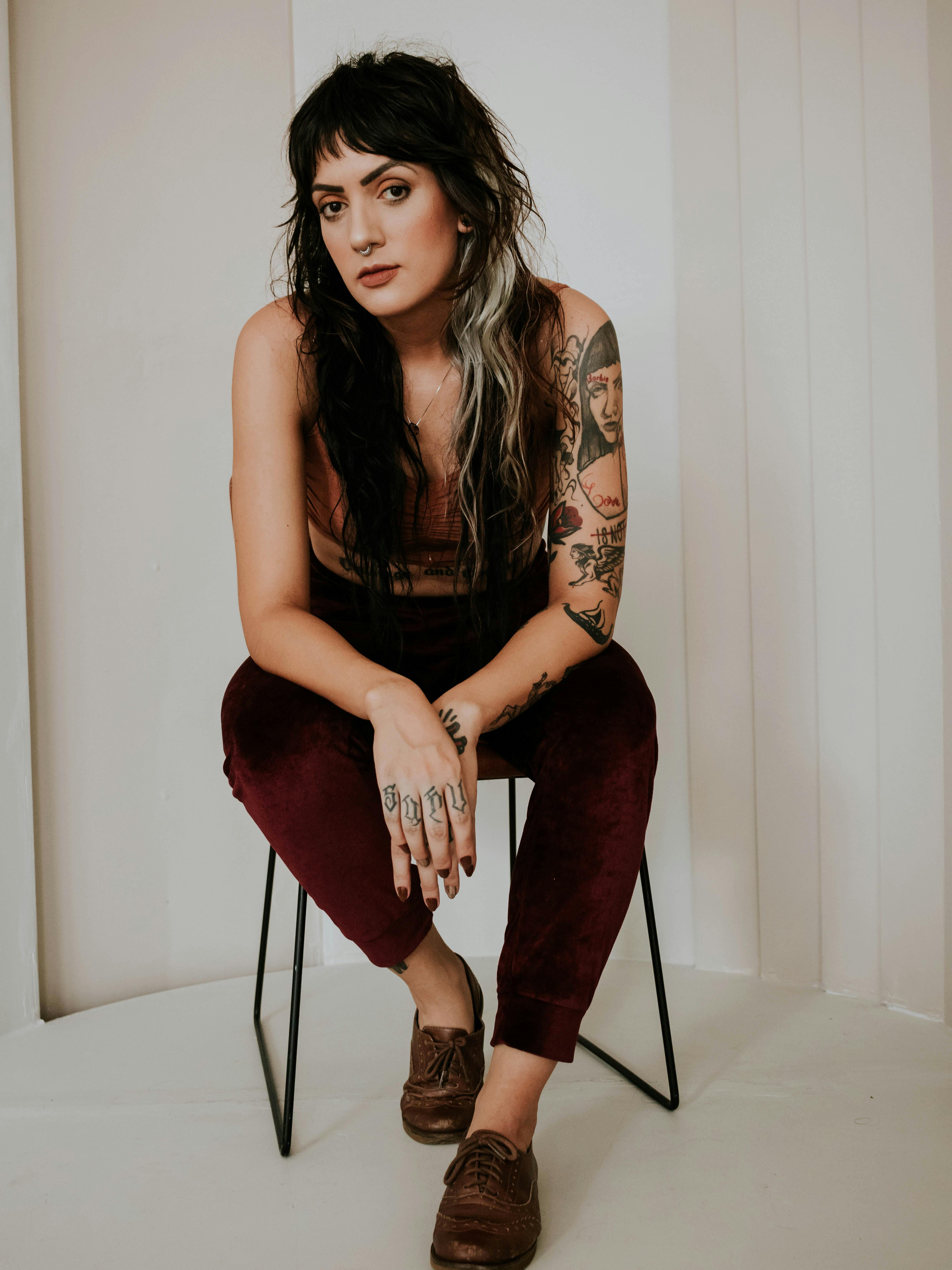 Portrait of a tattooed woman sitting pensively against a neutral background, indoors.