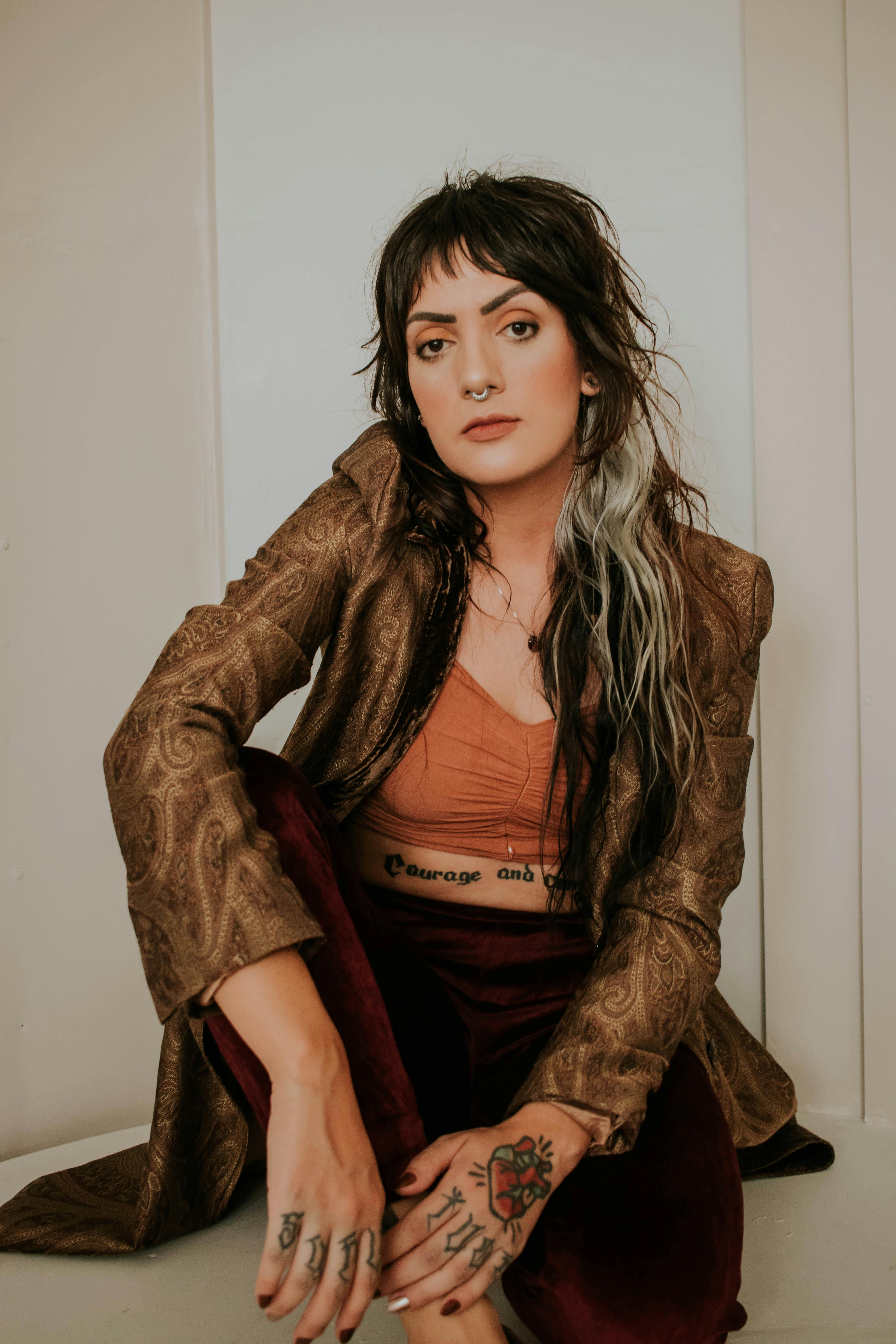 Portrait of a stylish woman indoors with tattoos and fashionable attire, displaying contemporary fashion and individuality.