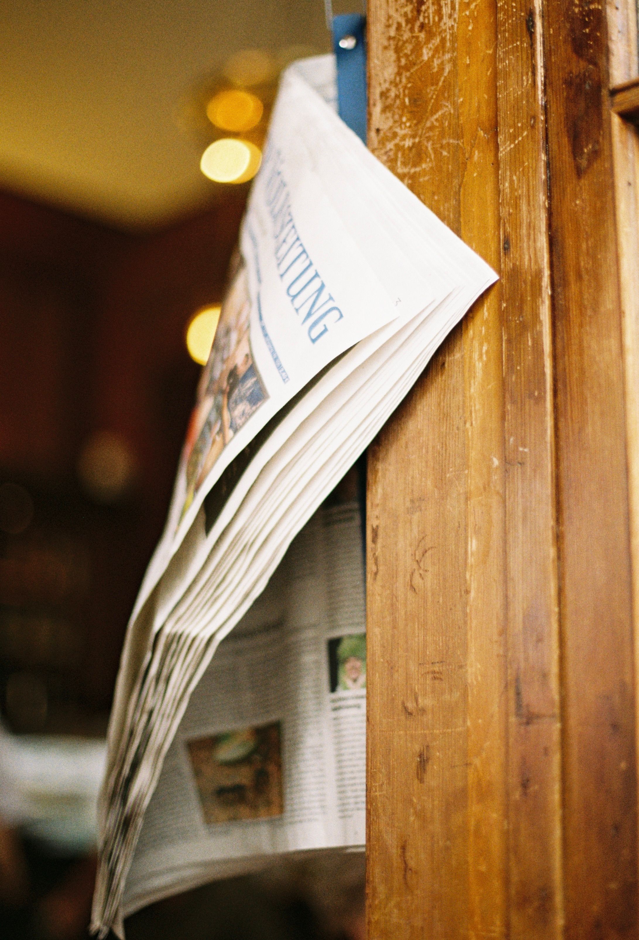 A folded newspaper hanging on a wooden wall inside a cozy room with warm lighting.