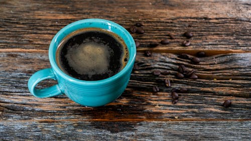 A steaming cup of coca tea with coca leaves scattered around it on a rustic wooden table.