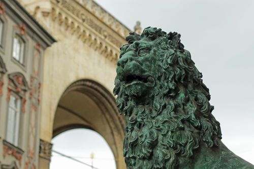 Free Majestic lion sculpture at Odeonsplatz, Munich with historical architecture backdrop. Stock Photo