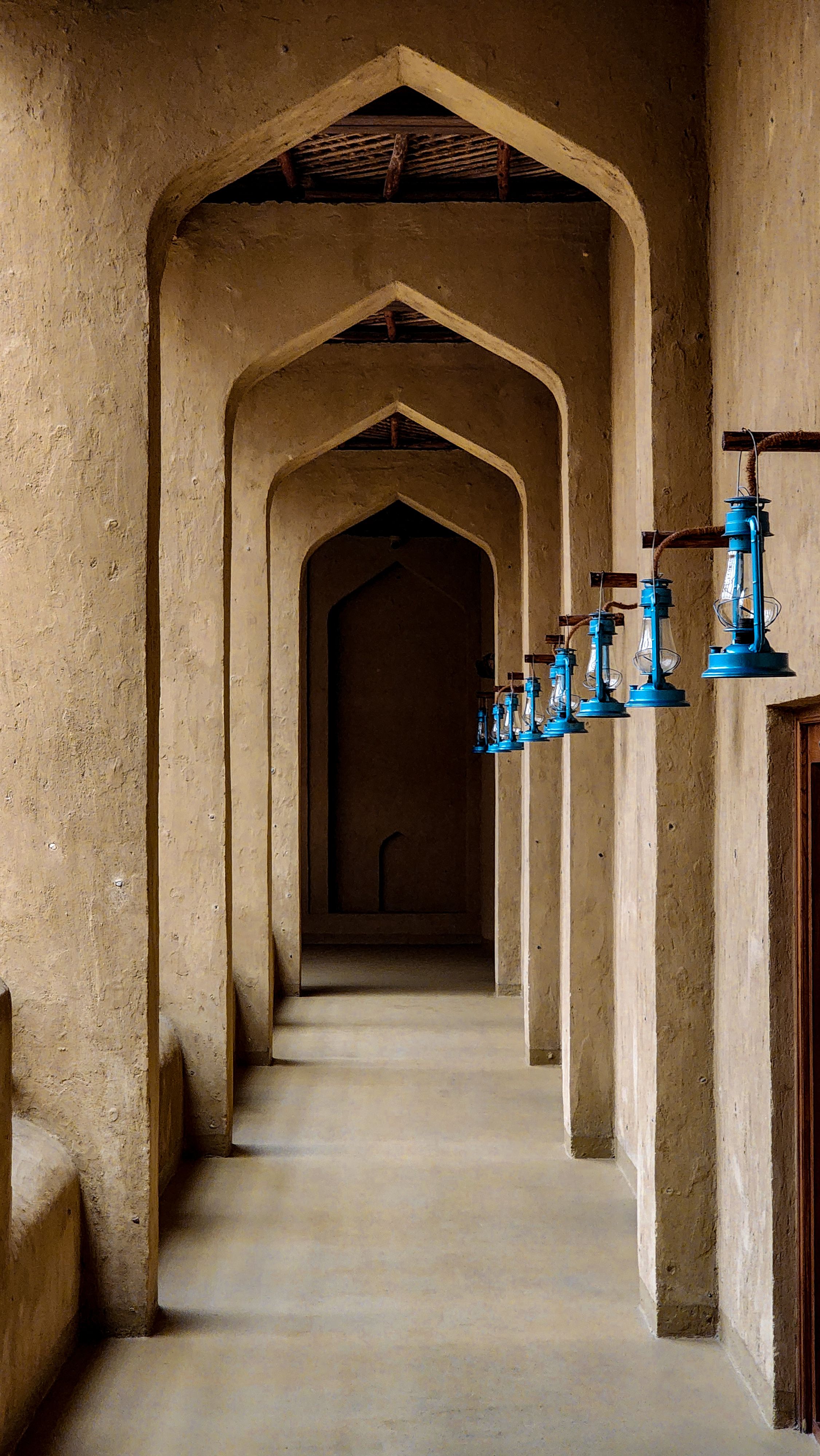 A traditional corridor in Oman with archways and blue lanterns, embodying Middle Eastern architecture.
