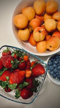 A vibrant assortment of strawberries, apricots, and blueberries in bowls, perfect for a healthy snack.
