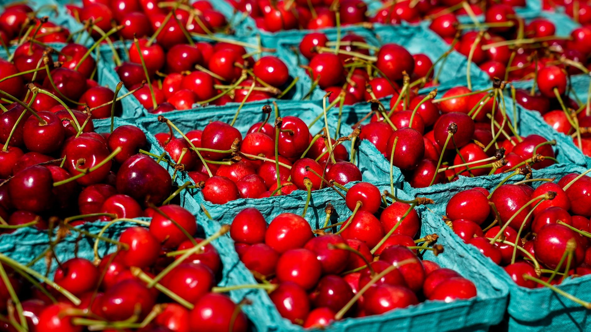 Vibrant red cherries in green cartons at a sunny farmers market. Fresh and ripe.