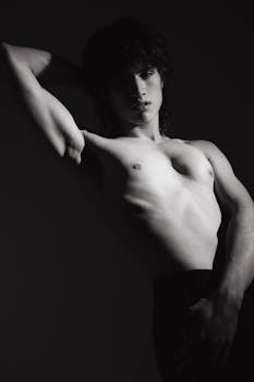 Striking black and white portrait of a young topless male posing confidently in dramatic lighting.