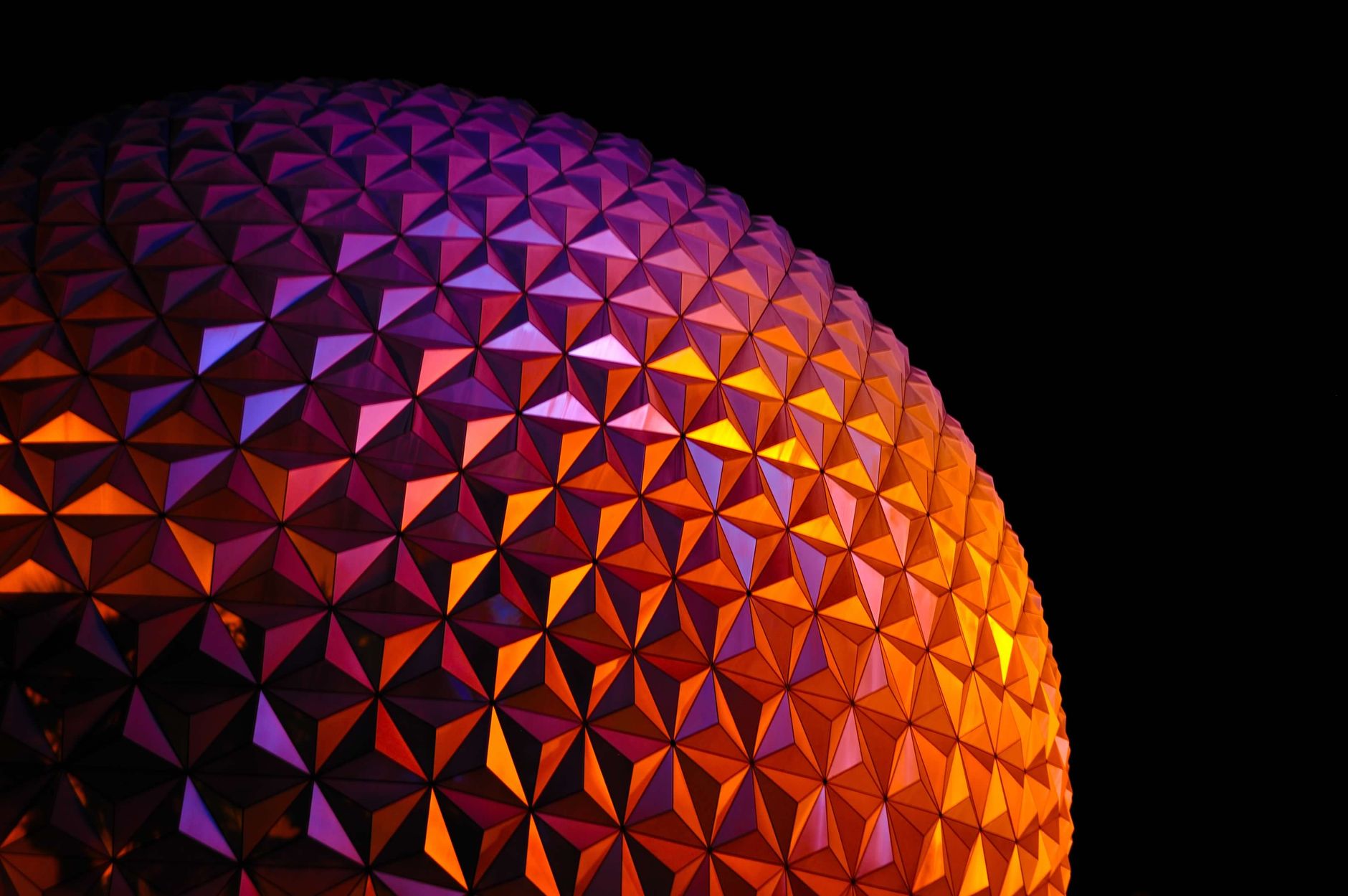 A vibrant geometric pattern dome illuminated in the dark, showcasing vivid purple and orange lighting.