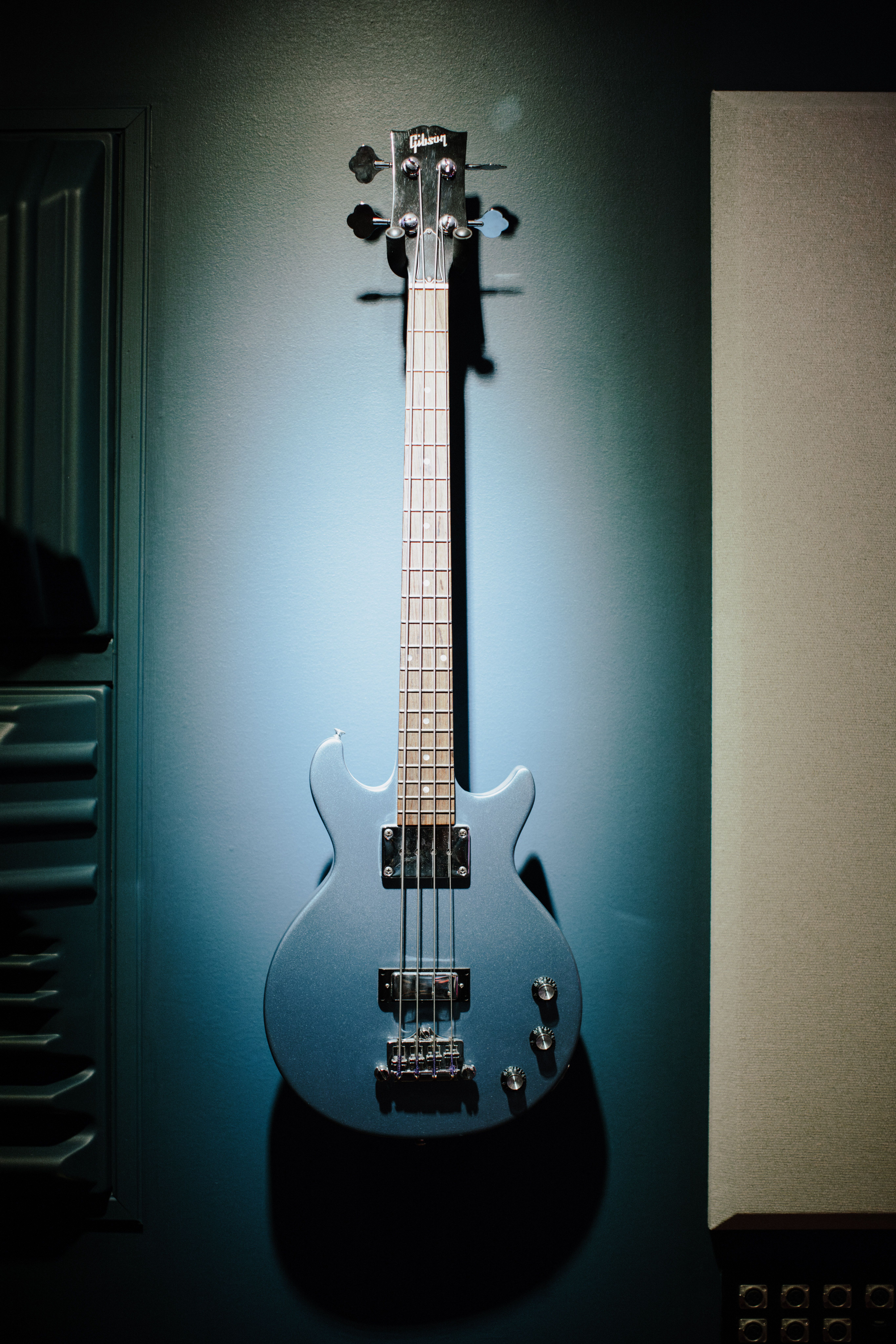A blue electric bass guitar hangs prominently on a wall, spotlighted for dramatic effect.