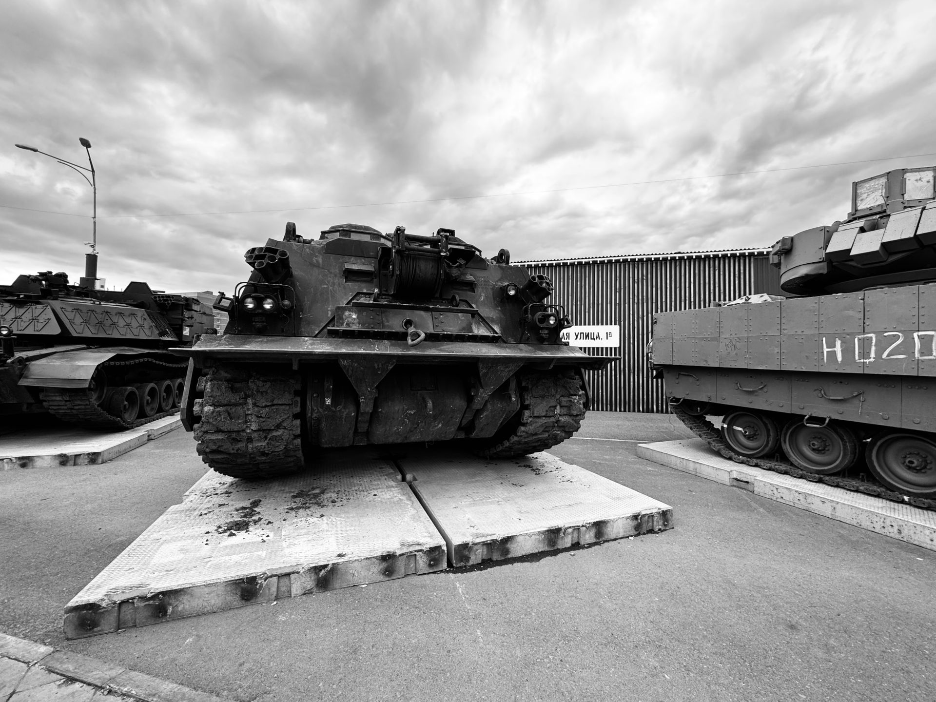 Black and white photo featuring outdoor display of military tanks under a cloudy sky.