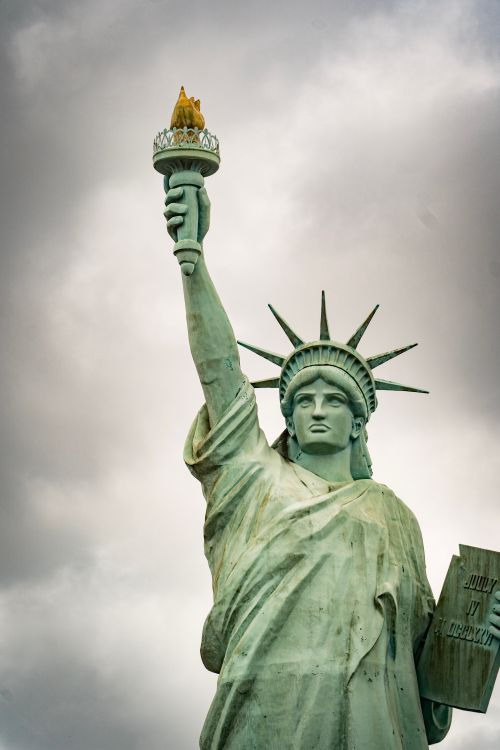 Free The Statue of Liberty stands tall under dramatic clouds in New York City. Stock Photo