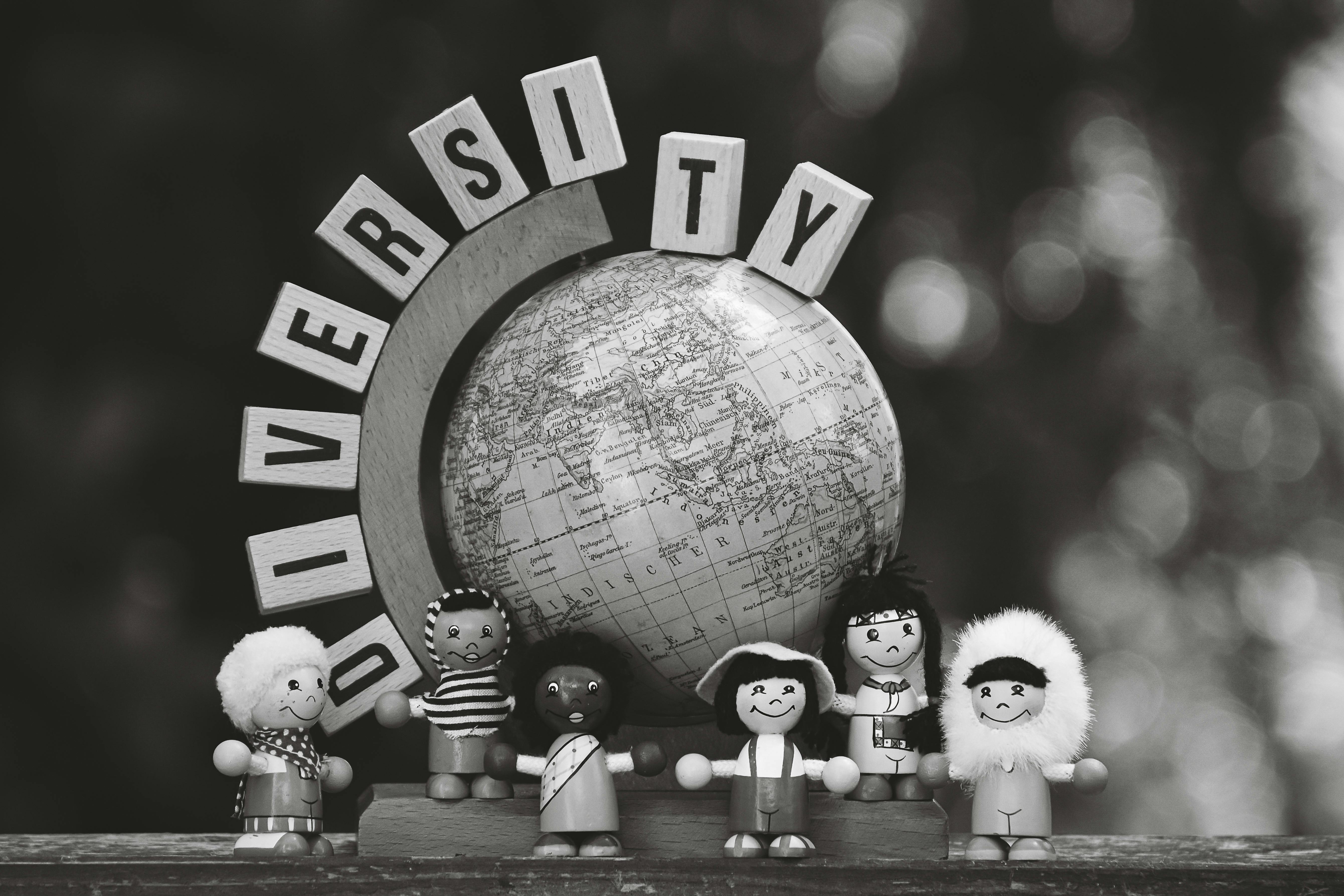 Free Black and white image of diverse wooden dolls and a globe representing cultural diversity. Stock Photo