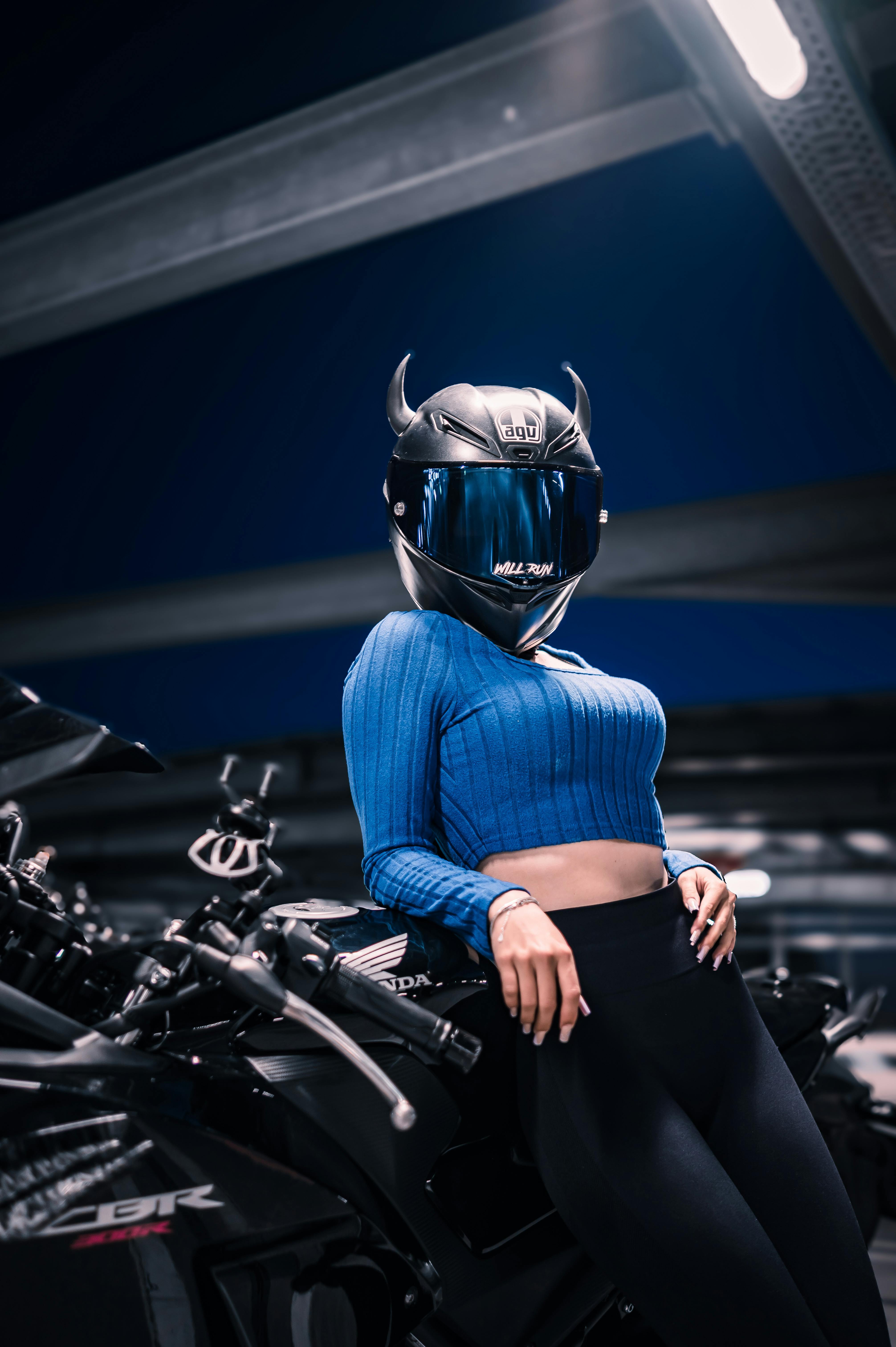 Woman wearing a stylish black helmet poses with a motorcycle indoors, showcasing modern biker fashion.