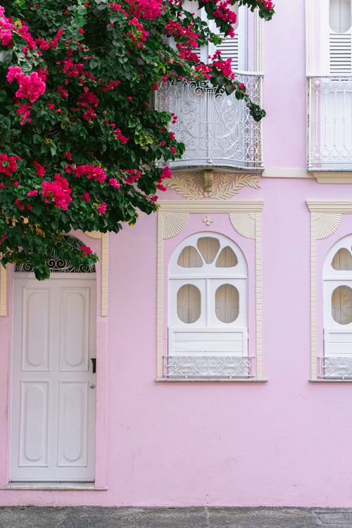 Kostenlos Ein malerisches rosafarbenes Gebäude, geschmückt mit leuchtenden Bougainvilleen, mit verzierten Balkonen und weißen Fenstern. Stock-Foto