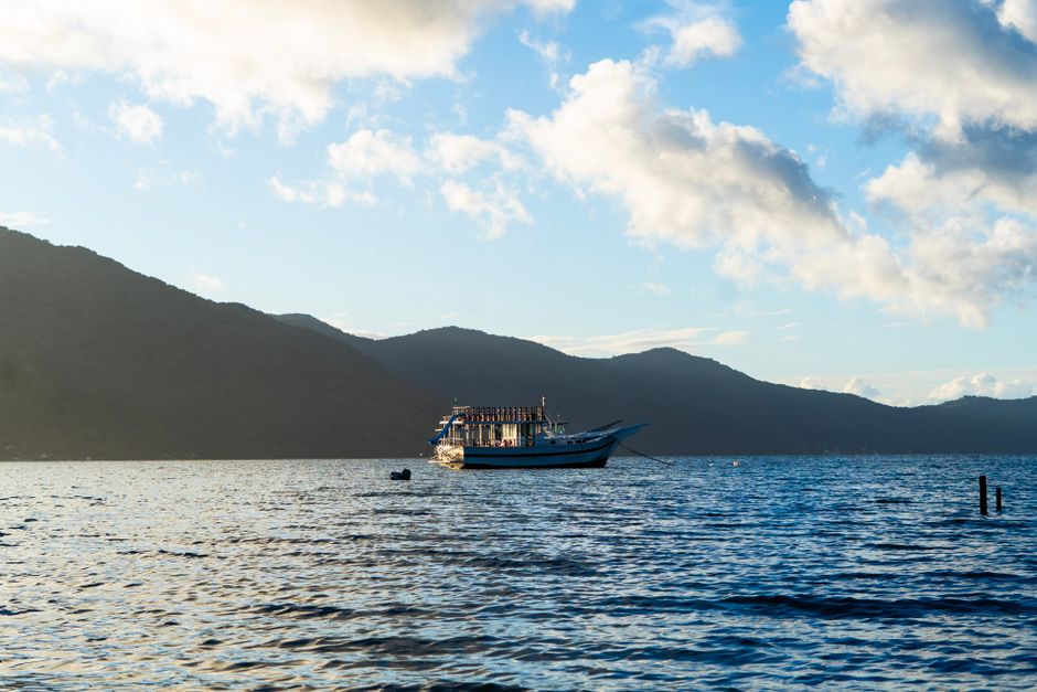 A picturesque view of a boat sailing on calm waters with mountains in the background at sunset.