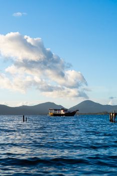 A serene boat floats on a calm lake with mountains and clouds at sunset, creating a peaceful scene.