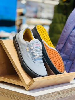 Modern gray sneakers with vibrant soles showcased on a wooden stand in a retail environment.