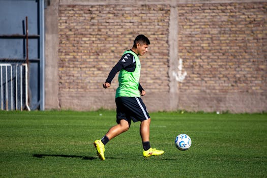 Teen soccer player in green jersey practicing on a sunny day outdoors.