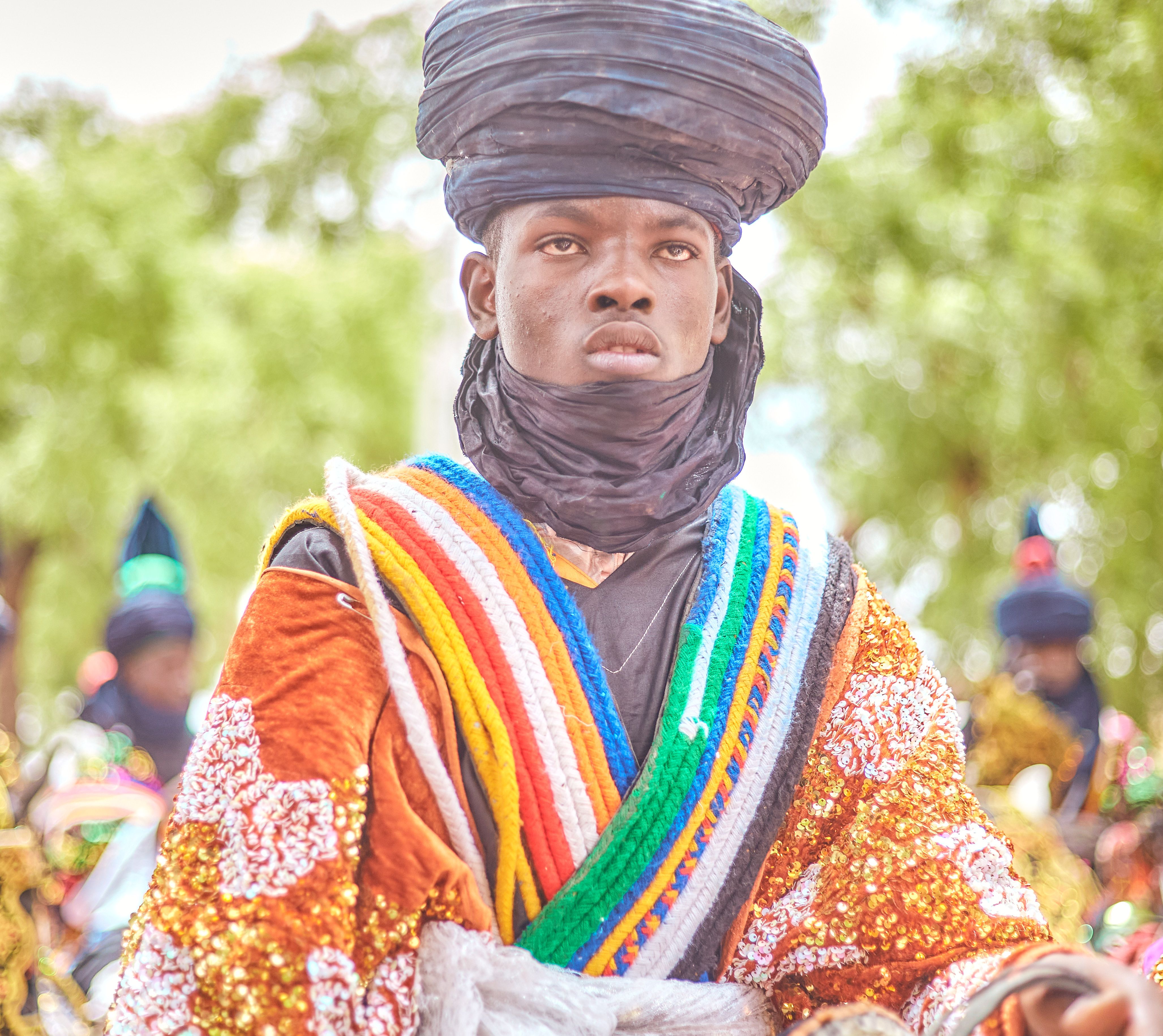 A man in colorful traditional African attire posing outdoors, showcasing cultural heritage.