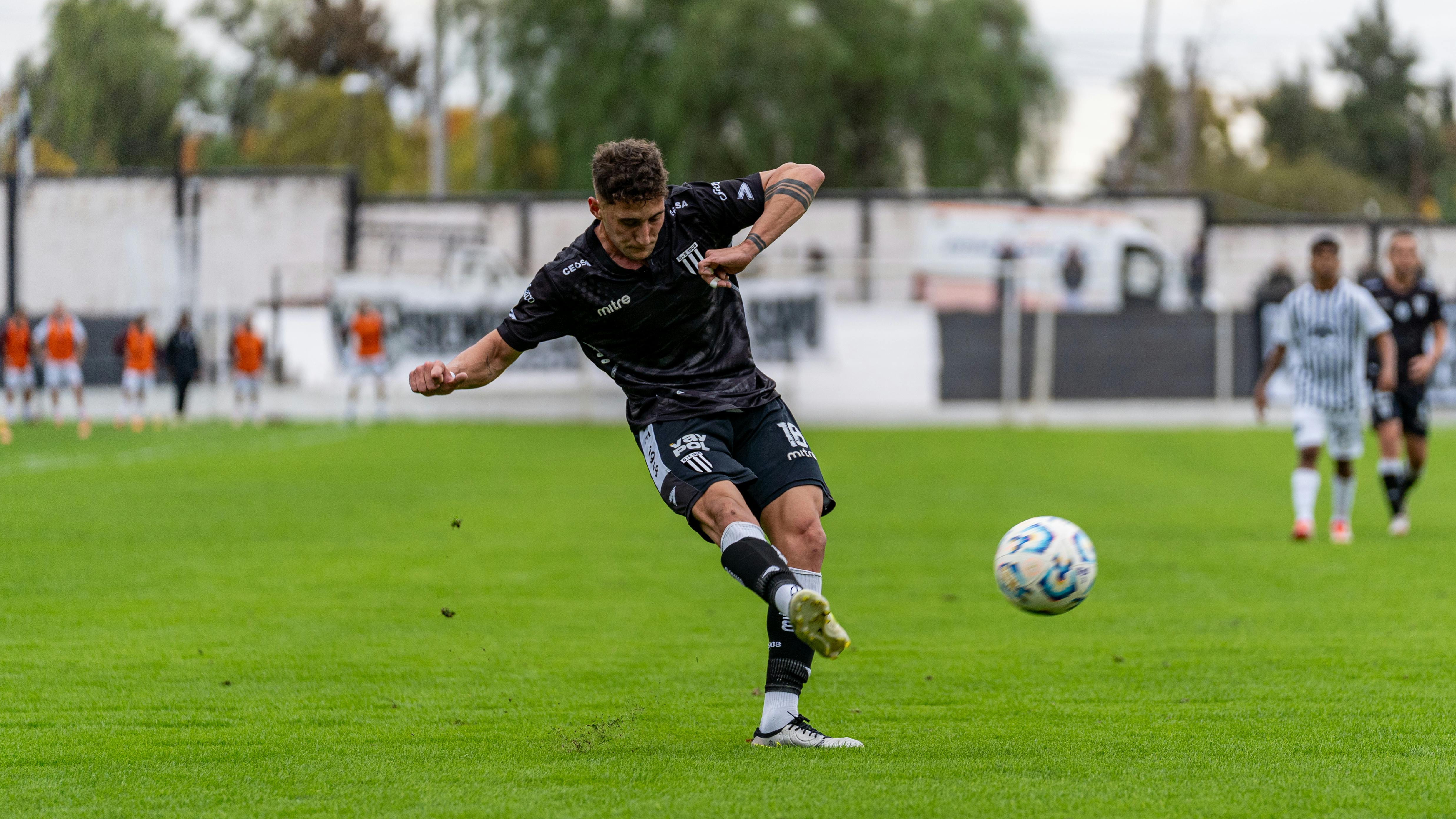 Football player kicking the ball with intensity during a match on a green field.