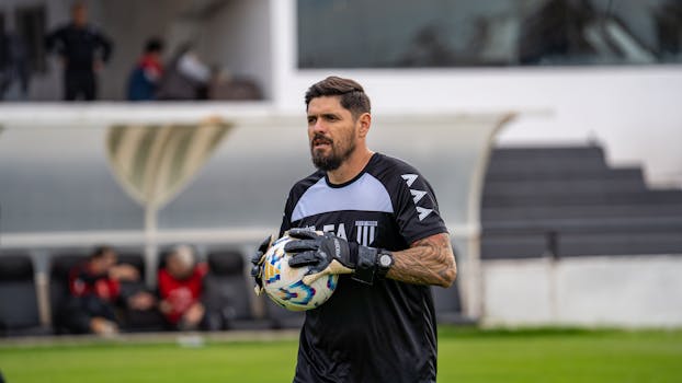 A soccer goalkeeper holding a ball during practice in an outdoor stadium setting.