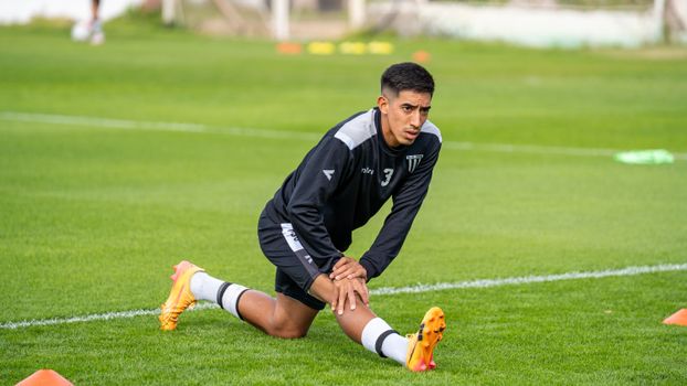 Soccer player preparing for practice by stretching in a grassy outdoor field.