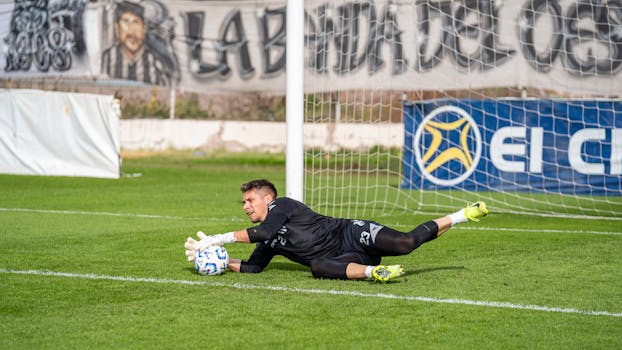 A goalkeeper in action making a dive save during a football match, showcasing skill and agility.