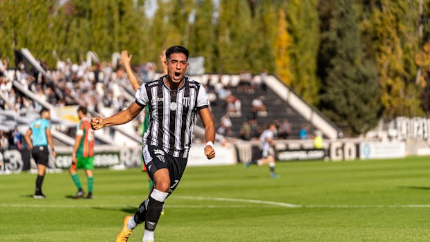 A football player in striped jersey jubilantly celebrates after scoring a goal during a match.