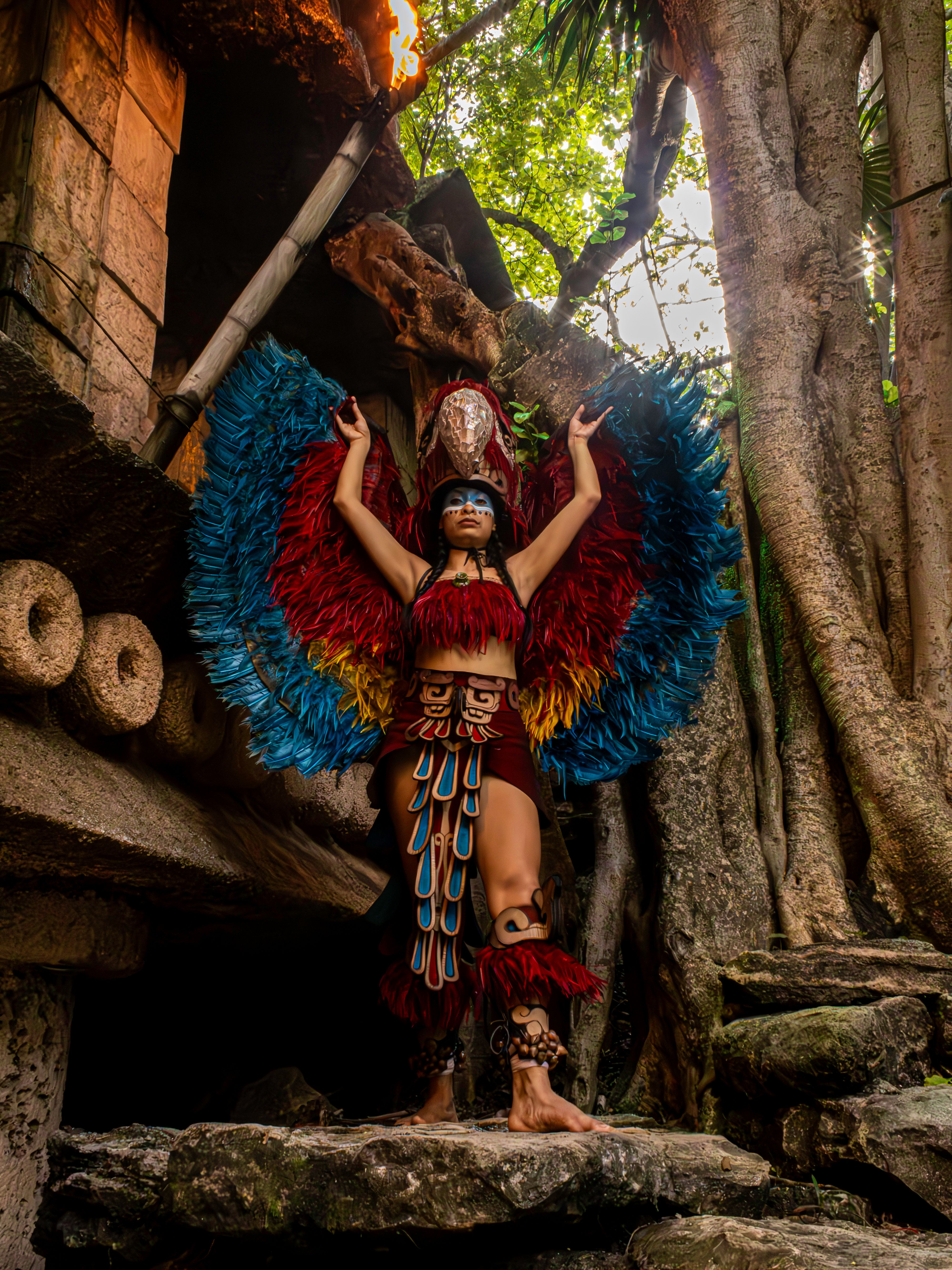 Indigenous warrior adorned in vibrant feathers poses amidst ancient jungle ruins.