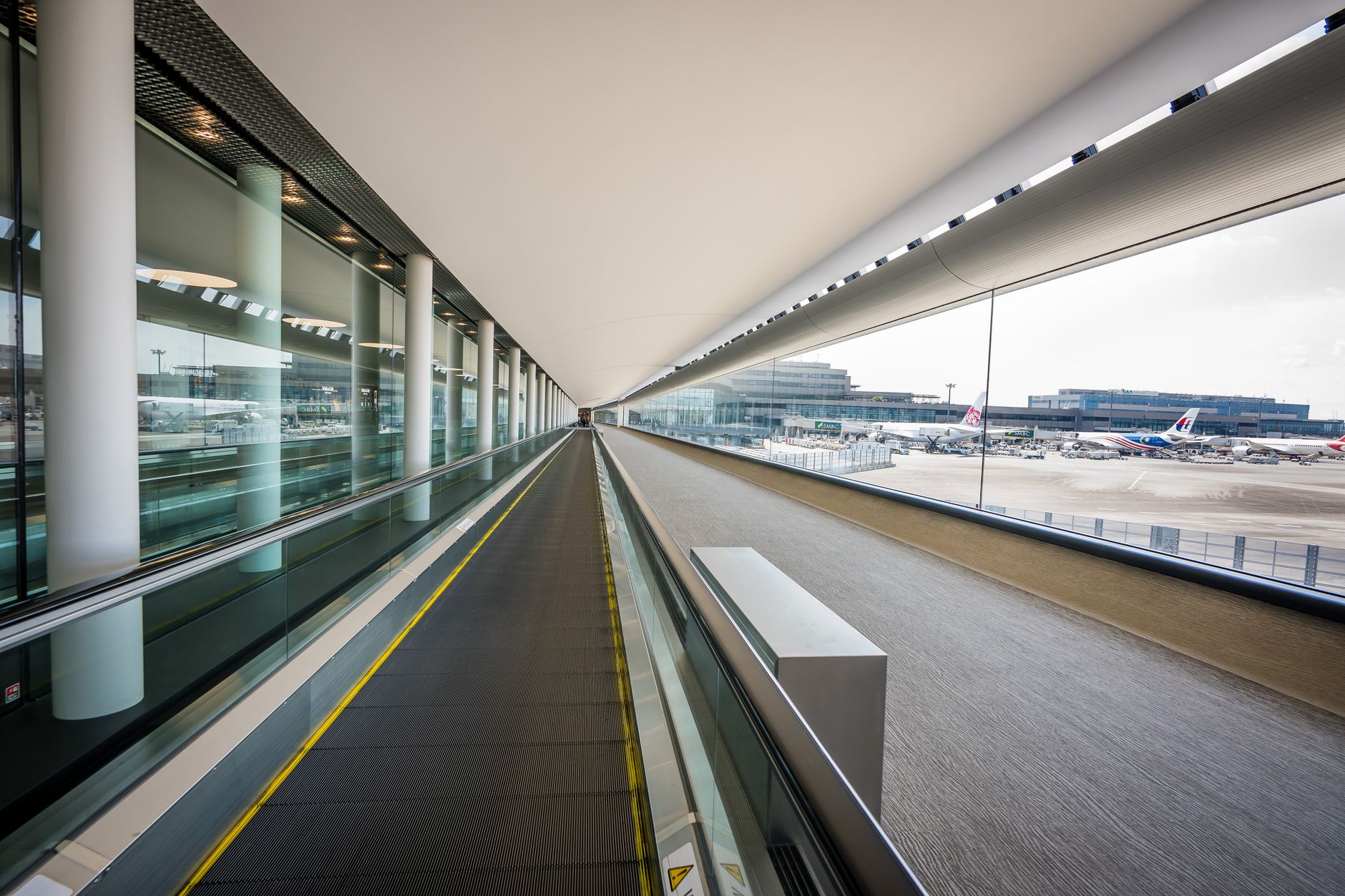 Sleek interior view of a Japanese airport terminal with a moving walkway and airplanes visible outside.