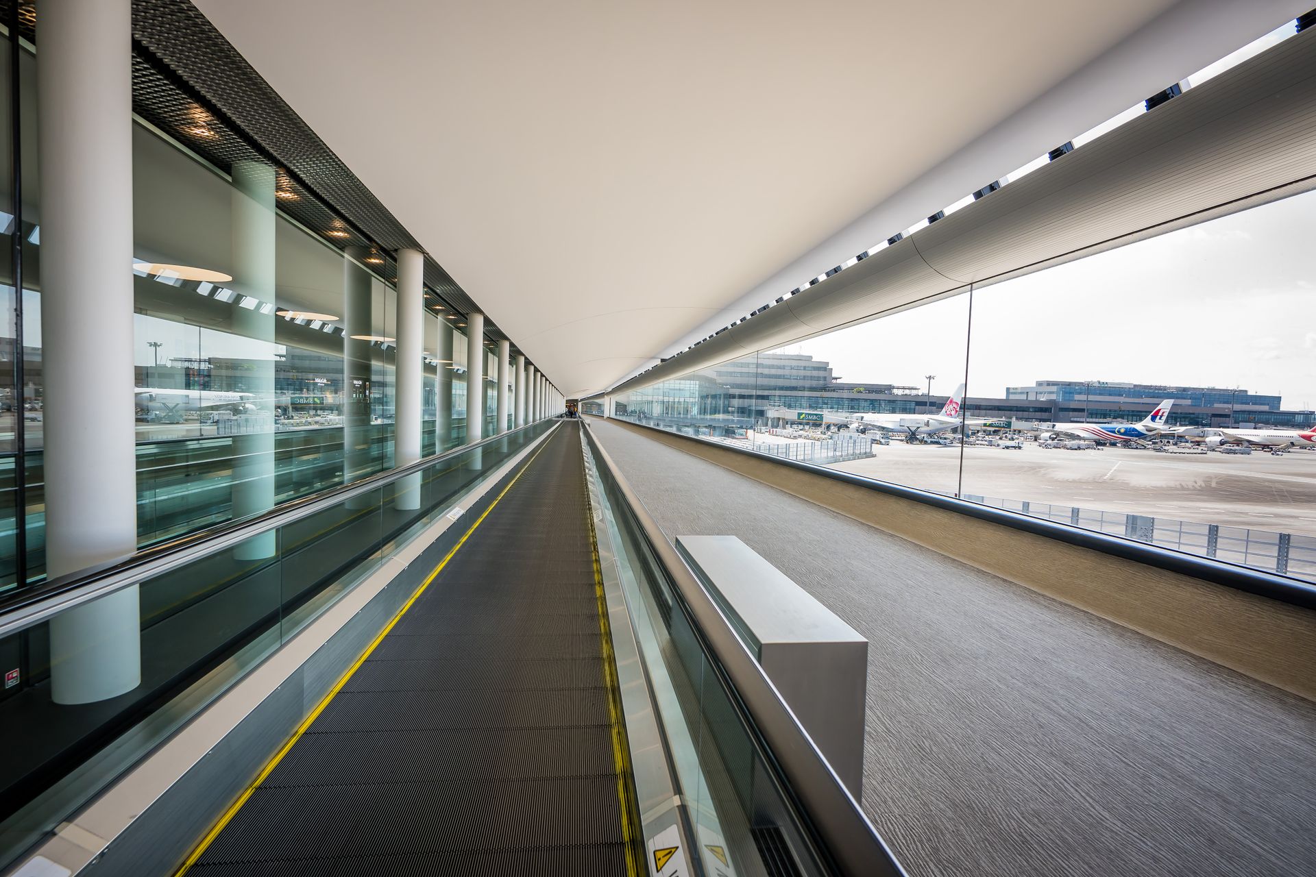 Sleek interior view of a Japanese airport terminal with a moving walkway and airplanes visible outside.
