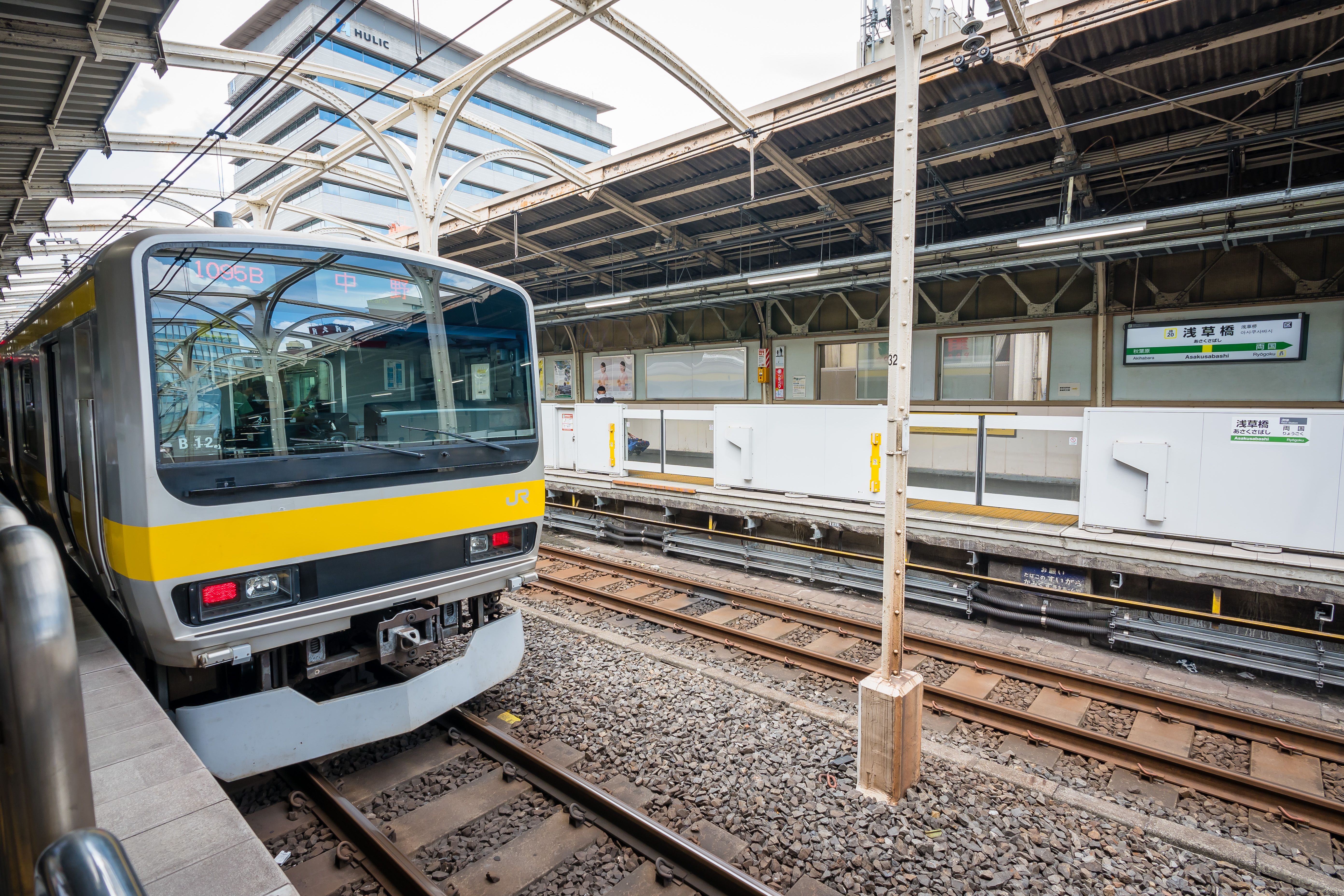 A modern yellow train at a bustling Tokyo train station during the day.
