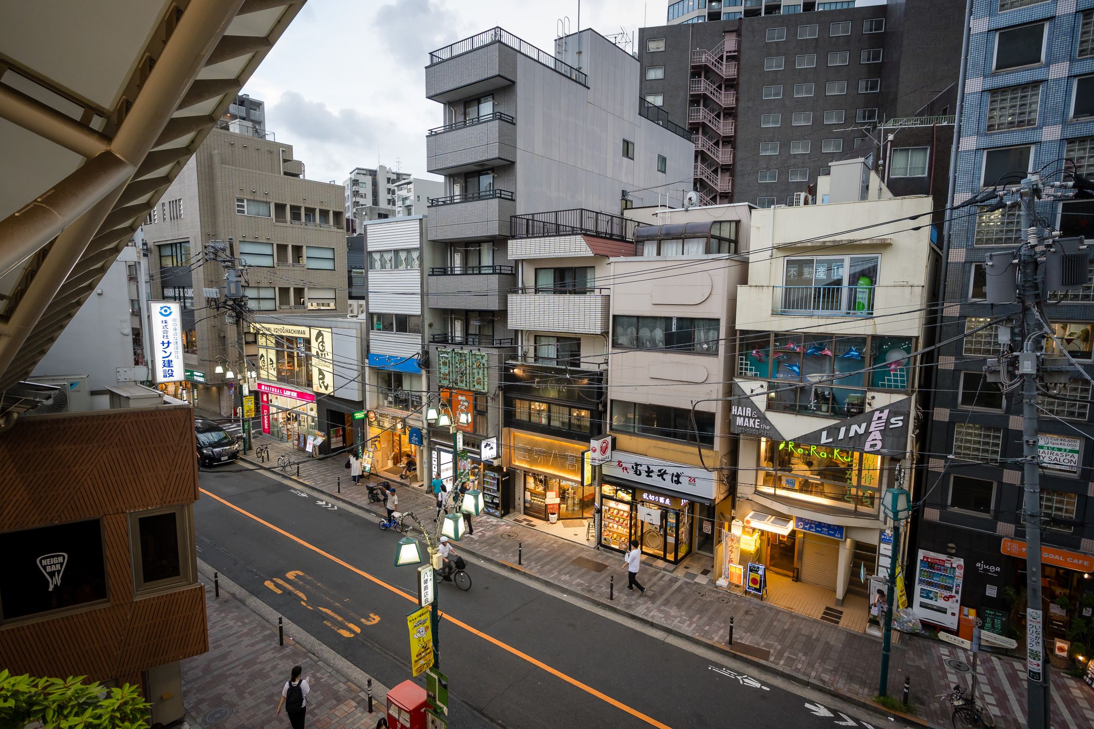 Street view of a vibrant Tokyo neighborhood at dusk, showcasing local shops and urban life.