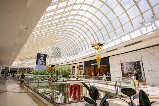 Spacious shopping mall interior with glass ceiling and luxury stores, captured in daylight.