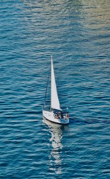 A sailboat peacefully cruises on vast blue ocean under clear skies, capturing tranquility.