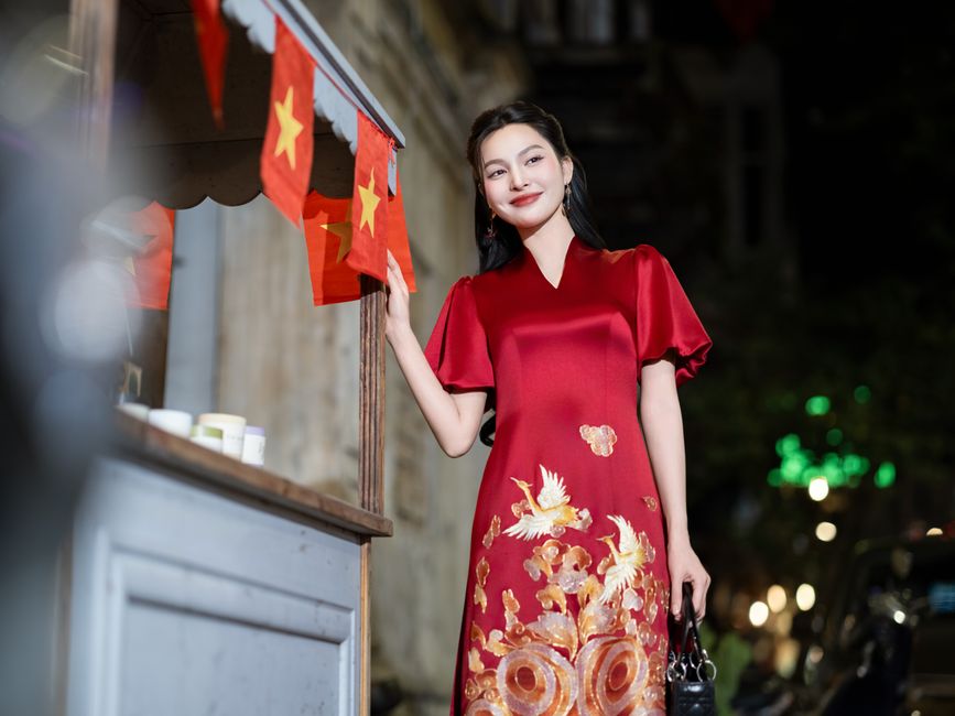 Woman in red traditional dress smiles by market stall with flags at night.