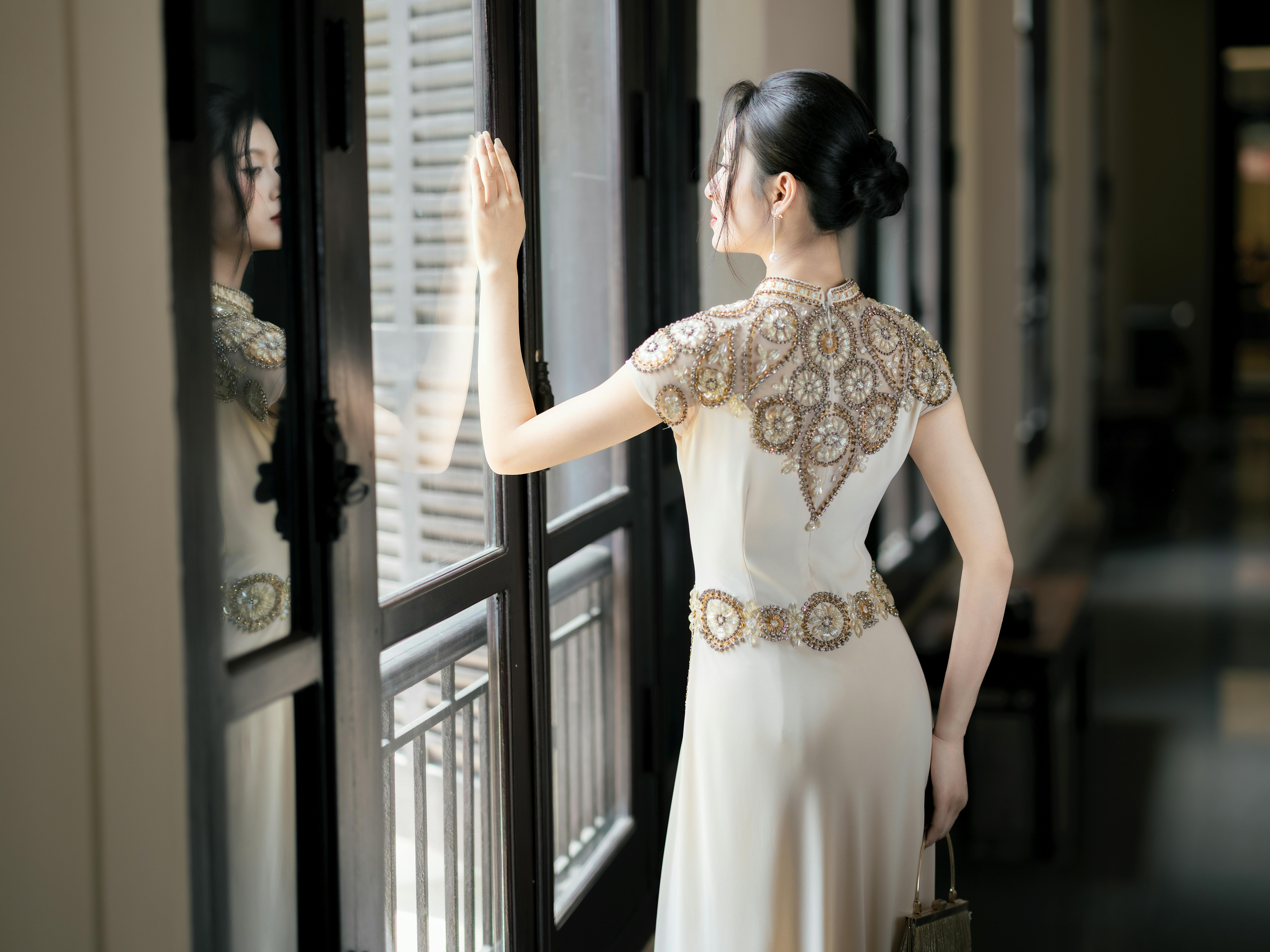 A woman in an ornate dress gazes out a window, reflecting elegance and nostalgia.