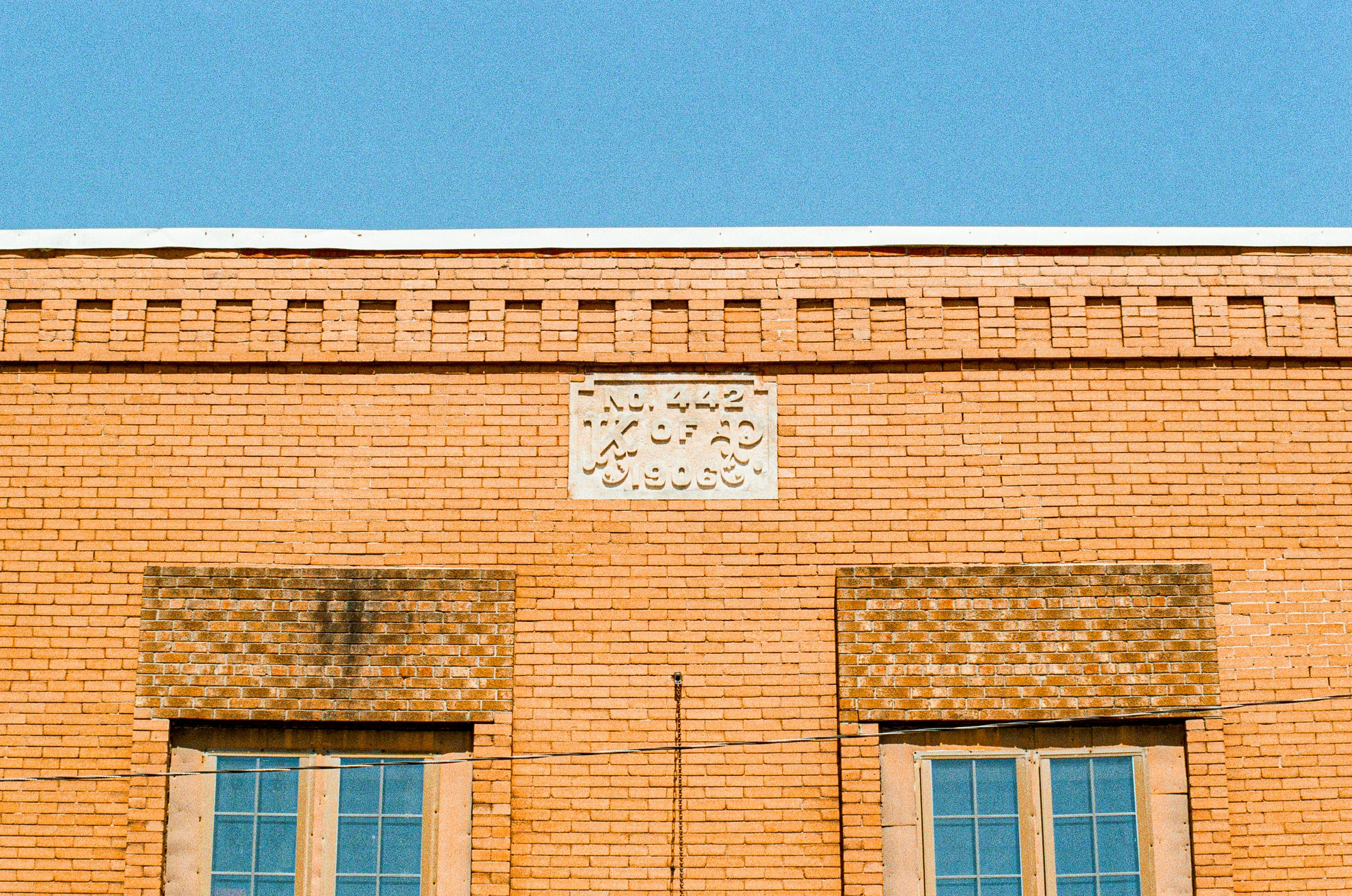 Δωρεάν Πρόσοψη ενός vintage κτιρίου από τούβλα με λεπτομερή τοιχοποιία και δύο παράθυρα κάτω από έναν καθαρό γαλάζιο ουρανό. Φωτογραφία από στοκ φωτογραφιών