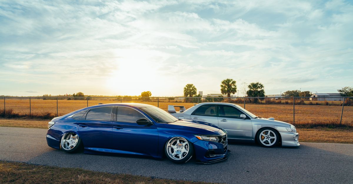 Two customized cars with lowered suspension on an open road during sunset.