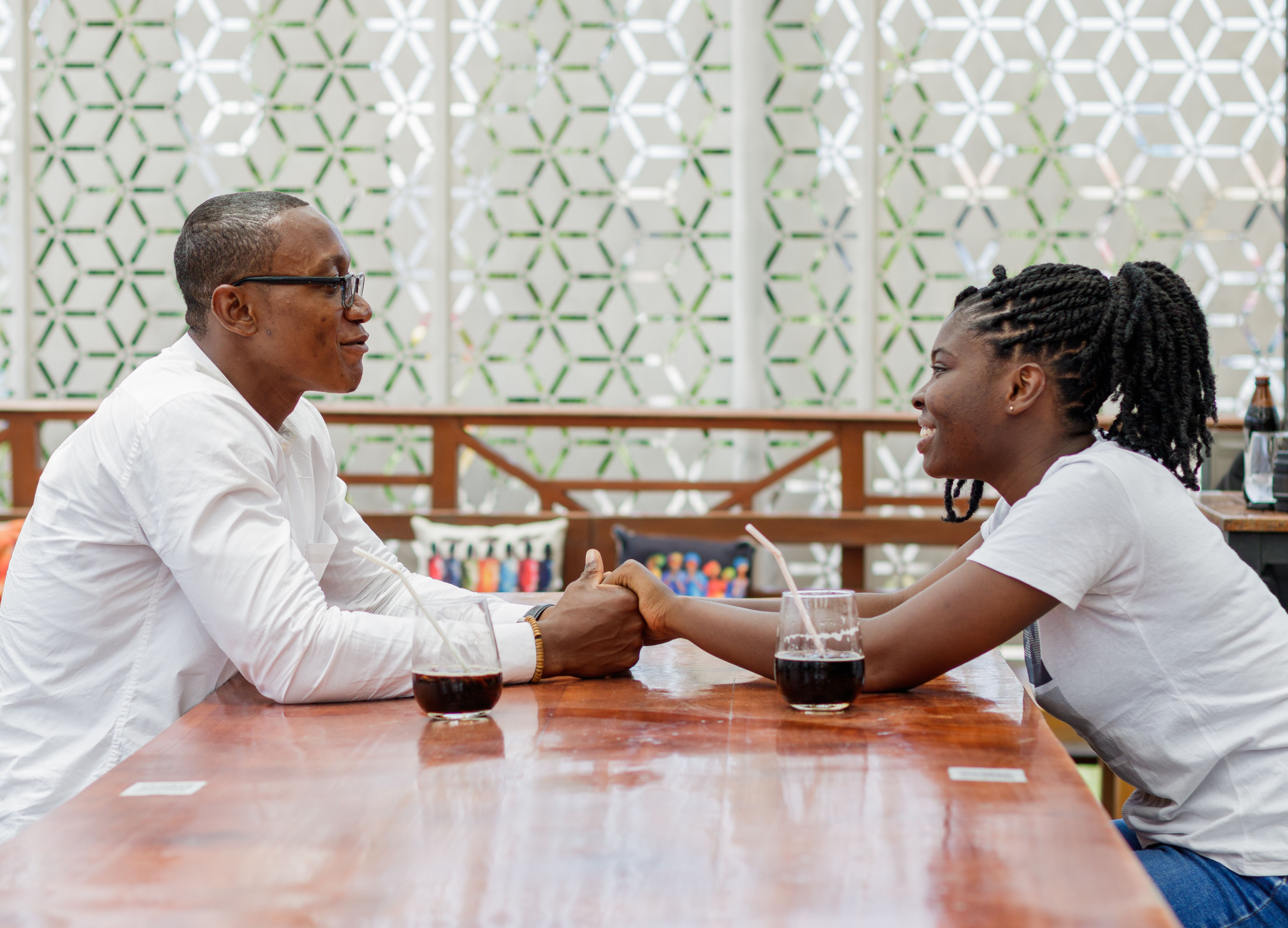 A loving couple holding hands at a cafe in Accra, Ghana, sharing a drink and a moment of happiness.