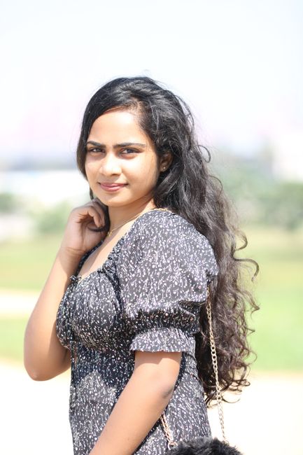 Portrait of a young woman with long dark hair posing outdoors on a sunny day.