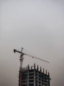 Urban skyline featuring a tower crane working on a high-rise building in overcast weather.