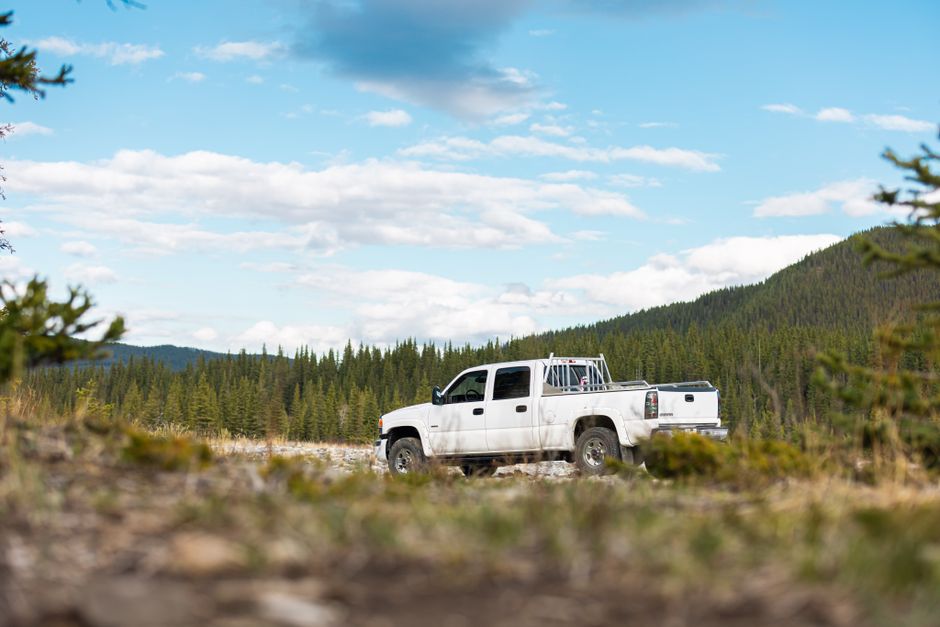 A white pickup truck parked offroad in a beautiful forest landscape under a clear sky.