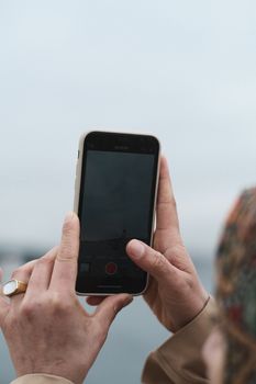 Close-up of hands holding a smartphone capturing the iconic Maiden's Tower against the cloudy sky.