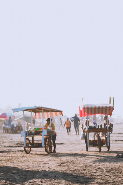 Free Beach vendors' carts offer snacks under striped canopies, bustling with beachgoers. Stock Photo