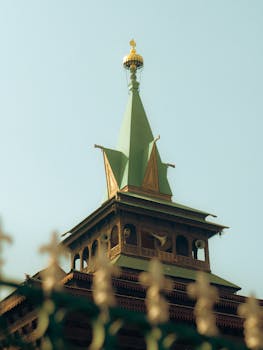 Ornate architectural minaret tower with green spire against a clear blue sky, showcasing intricate design.