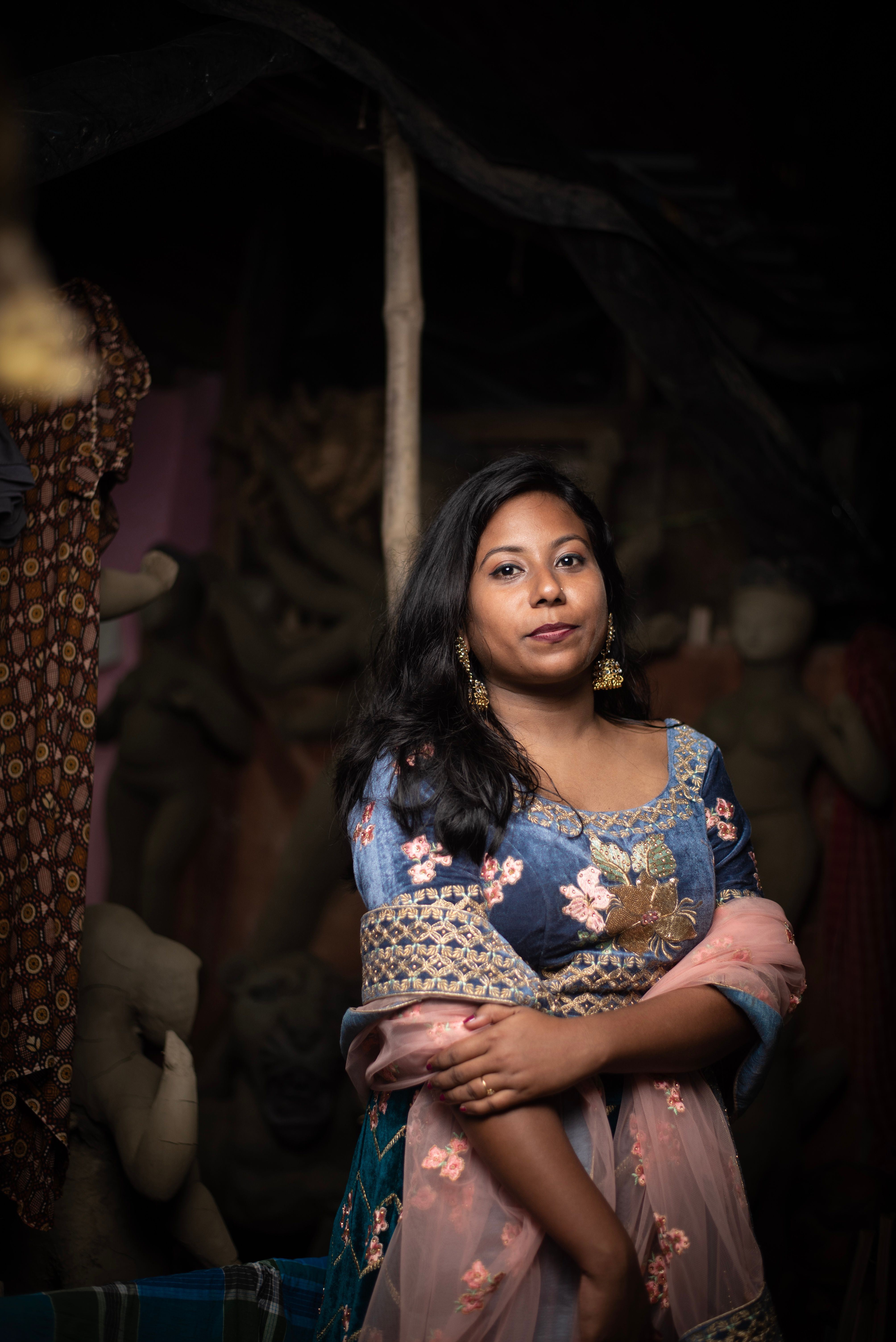 Elegant woman standing amidst handcrafted sculptures in a dimly lit workshop.