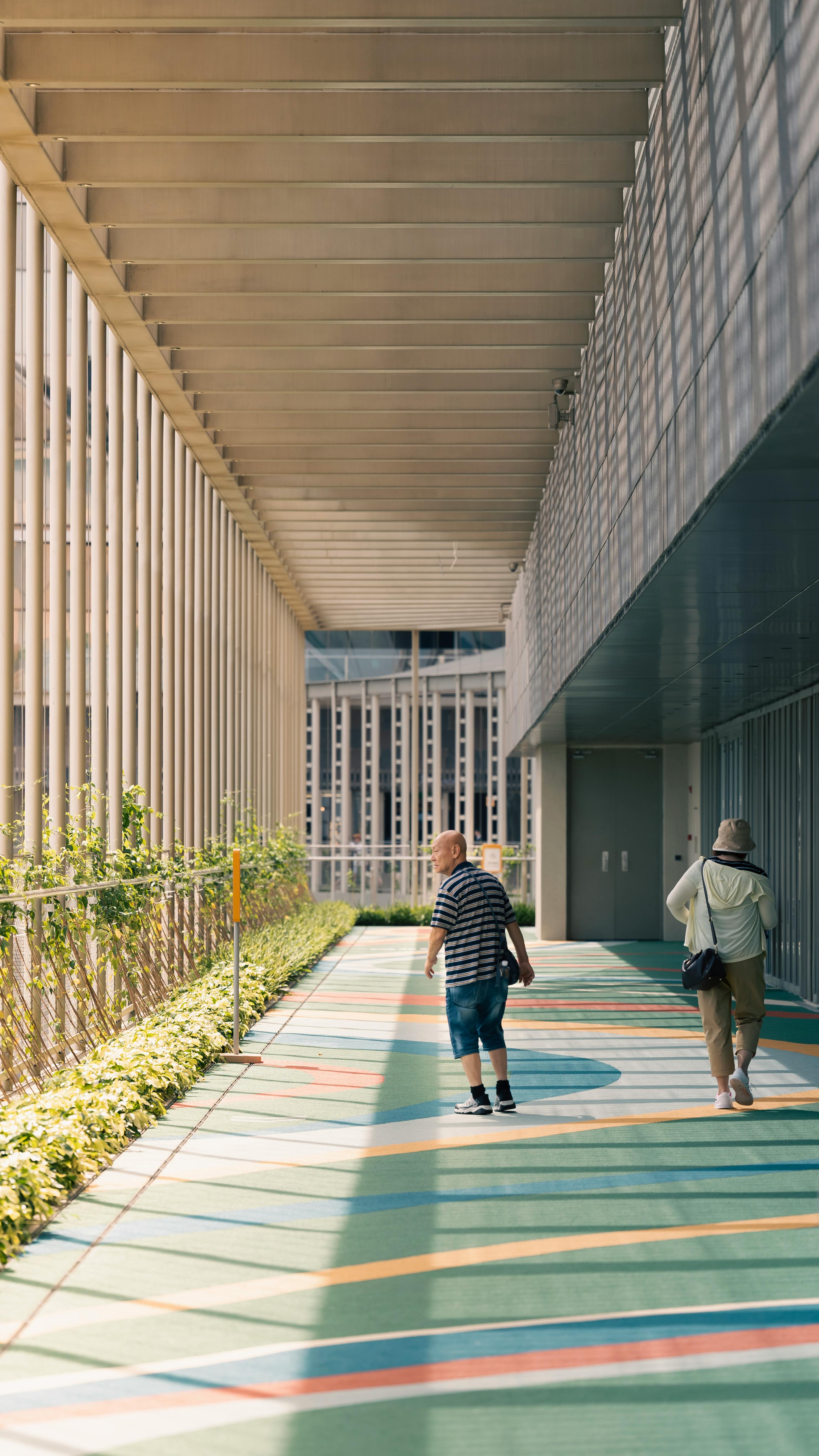 Two adults walking along a modern architectural corridor in daylight.