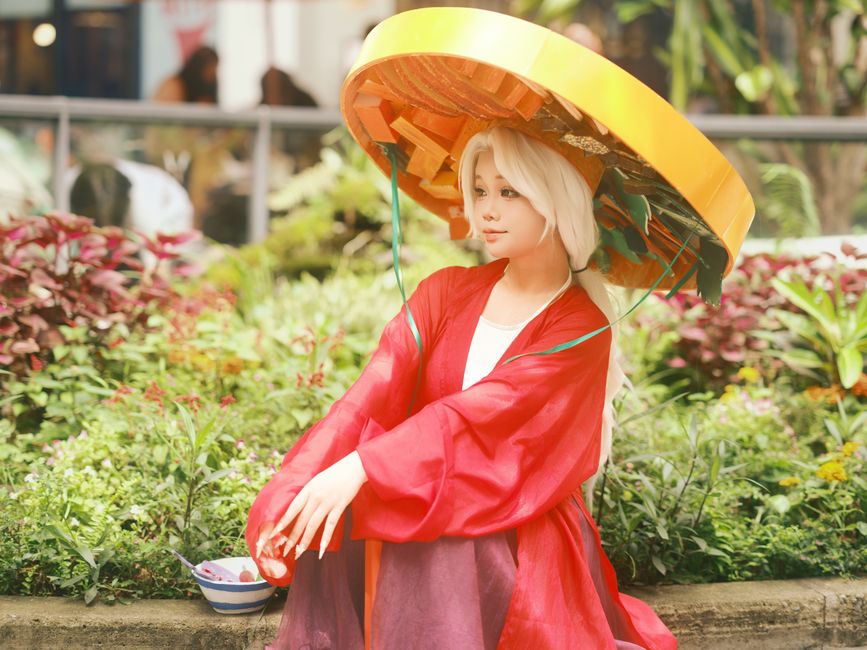 Cosplayer in traditional costume posing outdoors in a garden setting.