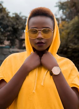 一位时尚的非洲女性戴着太阳镜和黄色连帽衫，在户外拍摄肖像，展现了现代风尚
